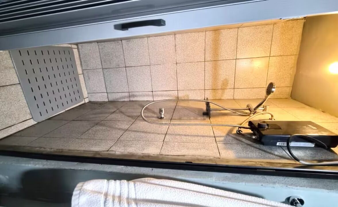 Un sol carrelé avec une grille métallique, un tuyau et un objet noir posé sur le sol.