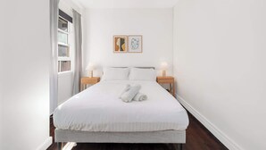 A hotel room with a bed, two bedside tables, a ceiling fan, and two wall-mounted artworks. - Boutique Apartment in Elizabeth Bay (Elizabeth Bay)