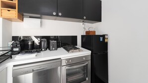 A compact kitchen with black cabinets, a stainless steel dishwasher, a built-in oven, a coffee maker, a toaster, and a refrigerator. - Boutique Apartment in Elizabeth Bay (Elizabeth Bay)