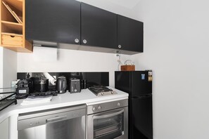 Eine kompakte Küche mit schwarzen Schränken, einem Edelstahl-Geschirrspüler, einem eingebauten Ofen, einer Kaffeemaschine, einem Toaster und einem Kühlschrank.