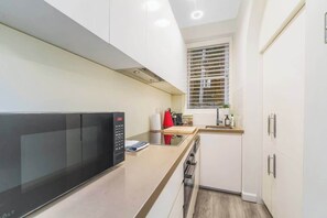 Eine moderne Küche mit weißen Schränken, einer schwarzen Mikrowelle und einem Fenster mit Jalousien.