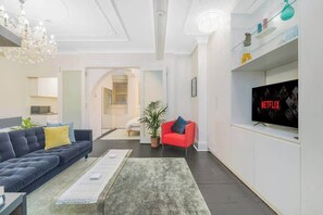 Ein Wohnzimmer mit einer Couch, einem roten Sessel, einem Couchtisch, einem Fernseher und einer Kristallleuchtre.