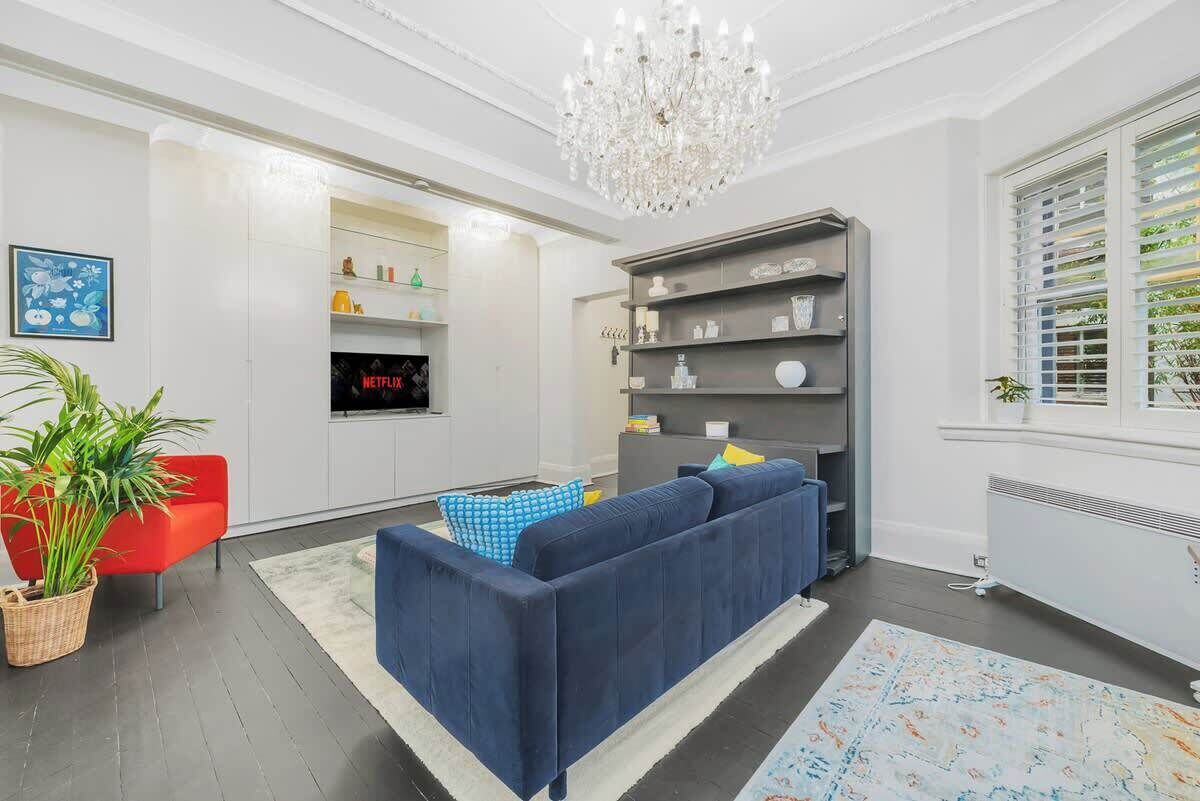 A modern living room with a blue sofa, a red chair, a chandelier, and a bookshelf.