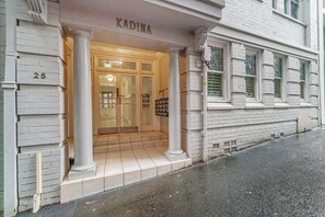 Ein Gebäudeeingang mit einem Schild, auf dem 'KADINA' steht, einem Doppeltür-Eingang und einer Treppe, die zum Eingang führt.