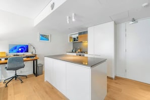Eine moderne Küche mit Kochinsel, Essbereich mit Holztisch und Stühlen sowie Arbeitsplatz mit Computer und Schreibtisch.