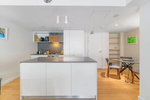 Eine moderne Küche mit weißen Schränken, einer zentralen Kochinsel und einem Essbereich mit einem Glastisch und Stühlen.