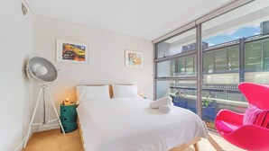 Moderni hotellihuone, jossa on suuri sänky, lattiavalaisin, suuri ikkuna ja vaaleanpunainen tuoli.