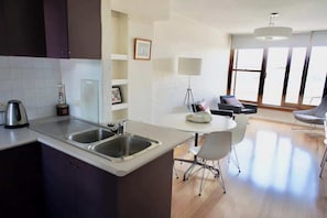 A modern kitchen with a central island, a dining area with a table and chairs, and large windows providing natural light. - 1 bedroom apartment with amazing view (Paddington)