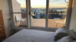 A bedroom with a bed, two pillows, a rolled towel, a chair, and a view of a cityscape through a large window. - 1 bedroom apartment with amazing view (Paddington)