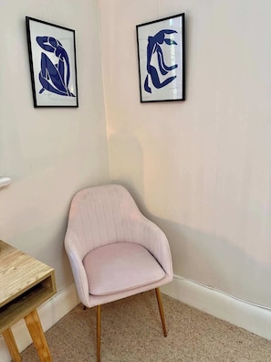 Ein Zimmer mit einem hellrosa Stuhl, einem Holztisch und zwei abstrakten Kunstwerken an der Wand.