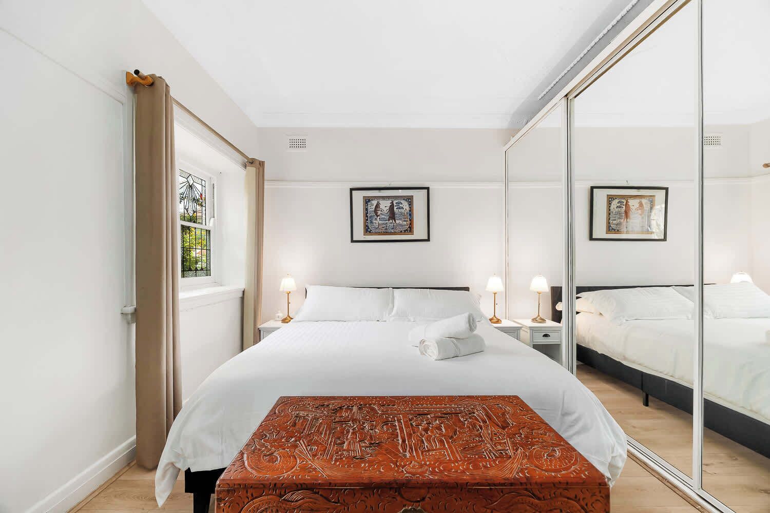 A bedroom with a large bed, bedside lamps, a mirror, and a wooden chest.