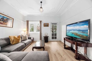 Ein Wohnzimmer mit grauem Sofa, einem Holztisch, einem Fernseher auf einem Holzboden und einem Fenster mit Landschaftsblick.