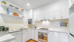 A modern kitchen with white cabinetry, a built-in microwave, a gas stove, and a dishwasher. - Spacious 2 bedroom apt with parking (Surry Hills)