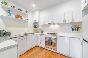 A modern kitchen with white cabinetry, a built-in microwave, a gas stove, and a dishwasher. - Spacious 2 bedroom apt with parking (Surry Hills)