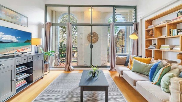 A living room with a sofa, a coffee table, a bookshelf, and a painting on the wall. - Spacious 2 bedroom apt with parking (Surry Hills)