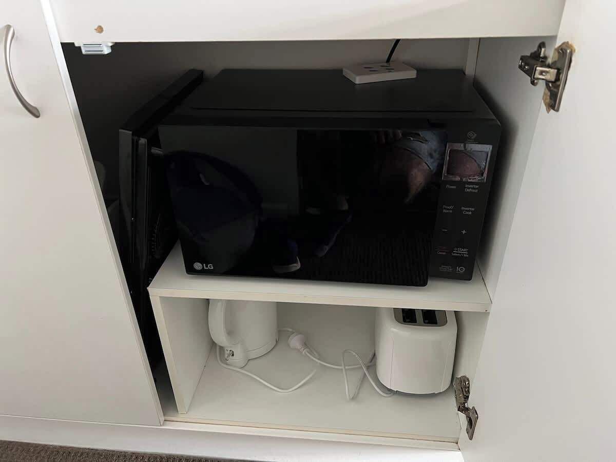 Eine Mikrowelle und eine Kaffeemaschine auf einem Regal in einem Küchenschrank.