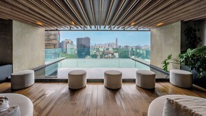 A modern interior with a wooden floor, a large window overlooking a cityscape, and several round seating areas. - The R Line I Sky Residences & Pool (Ciudad de México)