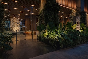 An indoor atrium with a modern design, featuring a glass wall, wooden slats, and lush greenery. - The R Line I Sky Residences & Pool (Ciudad de México)