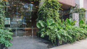 A modern building entrance with a glass door, a metal gate, and lush greenery including large-leafed plants. - The R Line I Sky Residences & Pool (Ciudad de México)