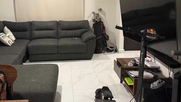 A living room with a grey sofa, a TV, a desk with a computer, and a golf bag.