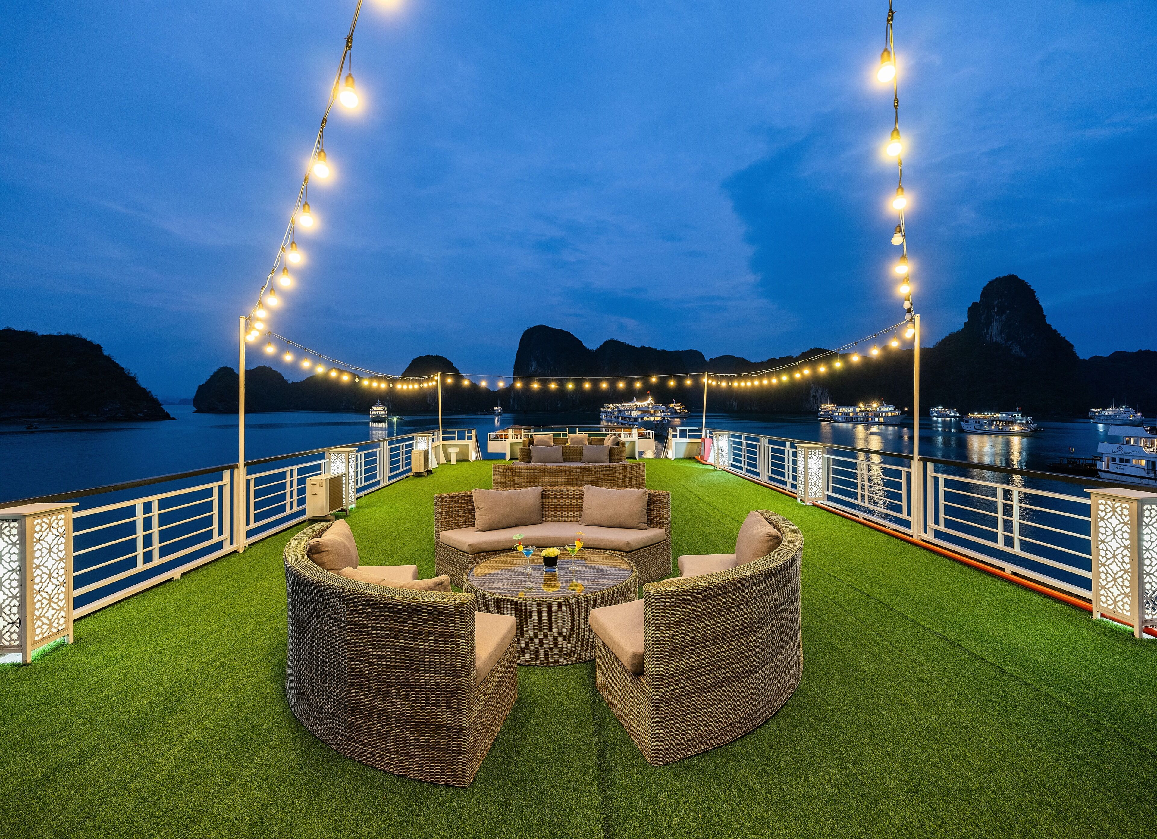 A rooftop deck with outdoor furniture, string lights, and a view of the water and mountains.