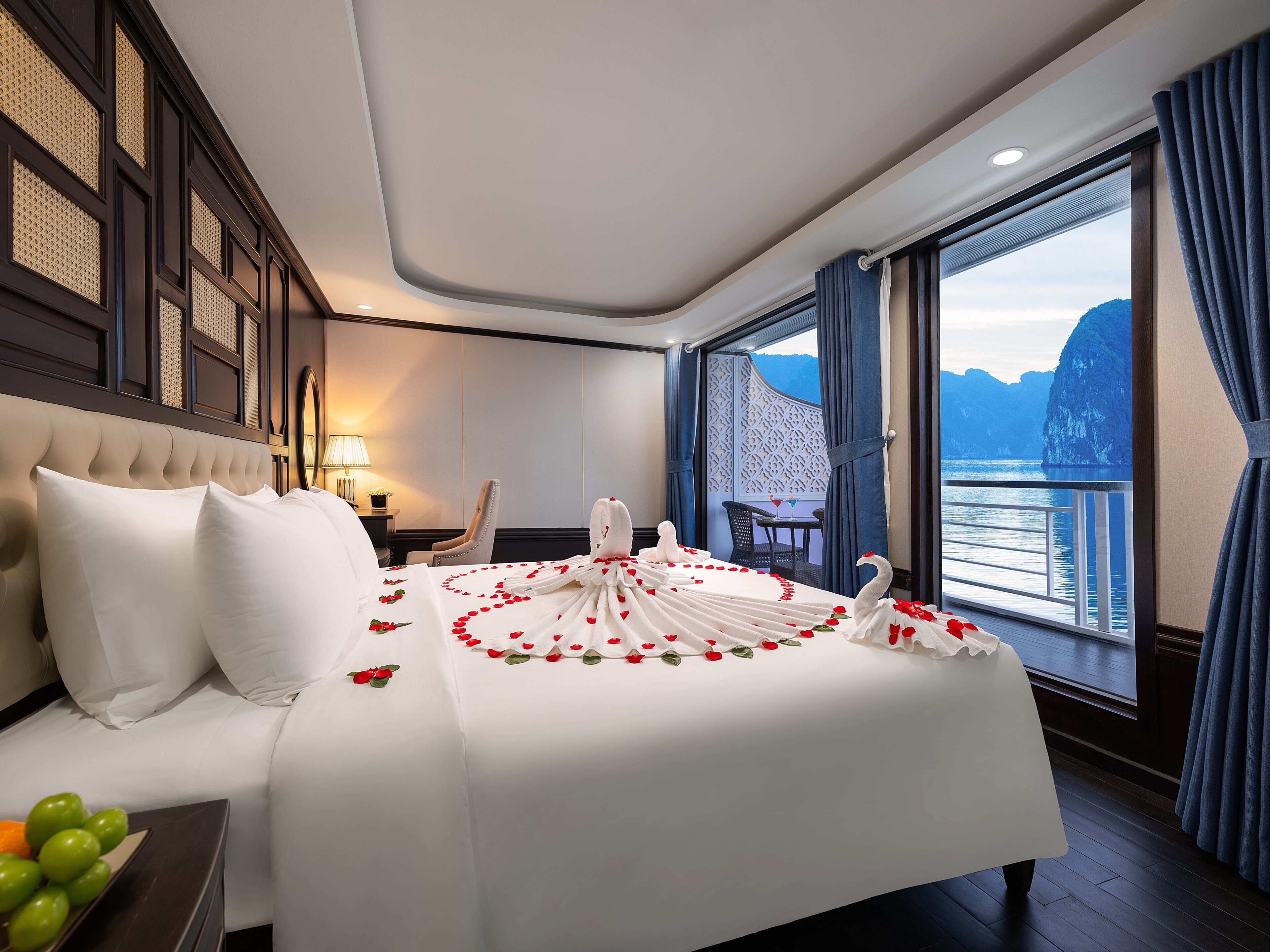 A hotel room with a bed, a nightstand, a lamp, a chair, a table with a glass and a bottle, and a view of the sea.