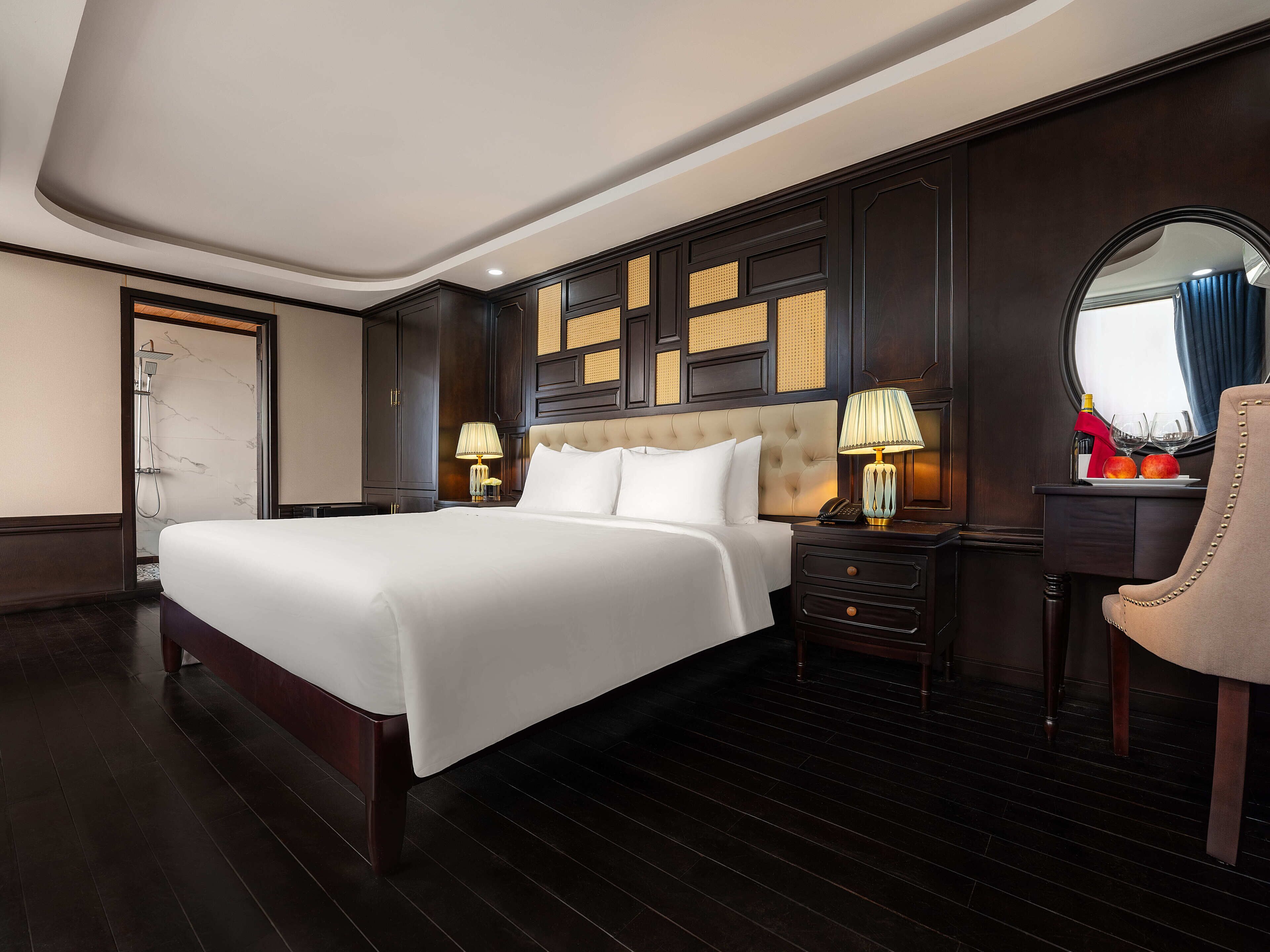 A hotel room with a large bed, a bedside table with a lamp, a mirror, and a nightstand.