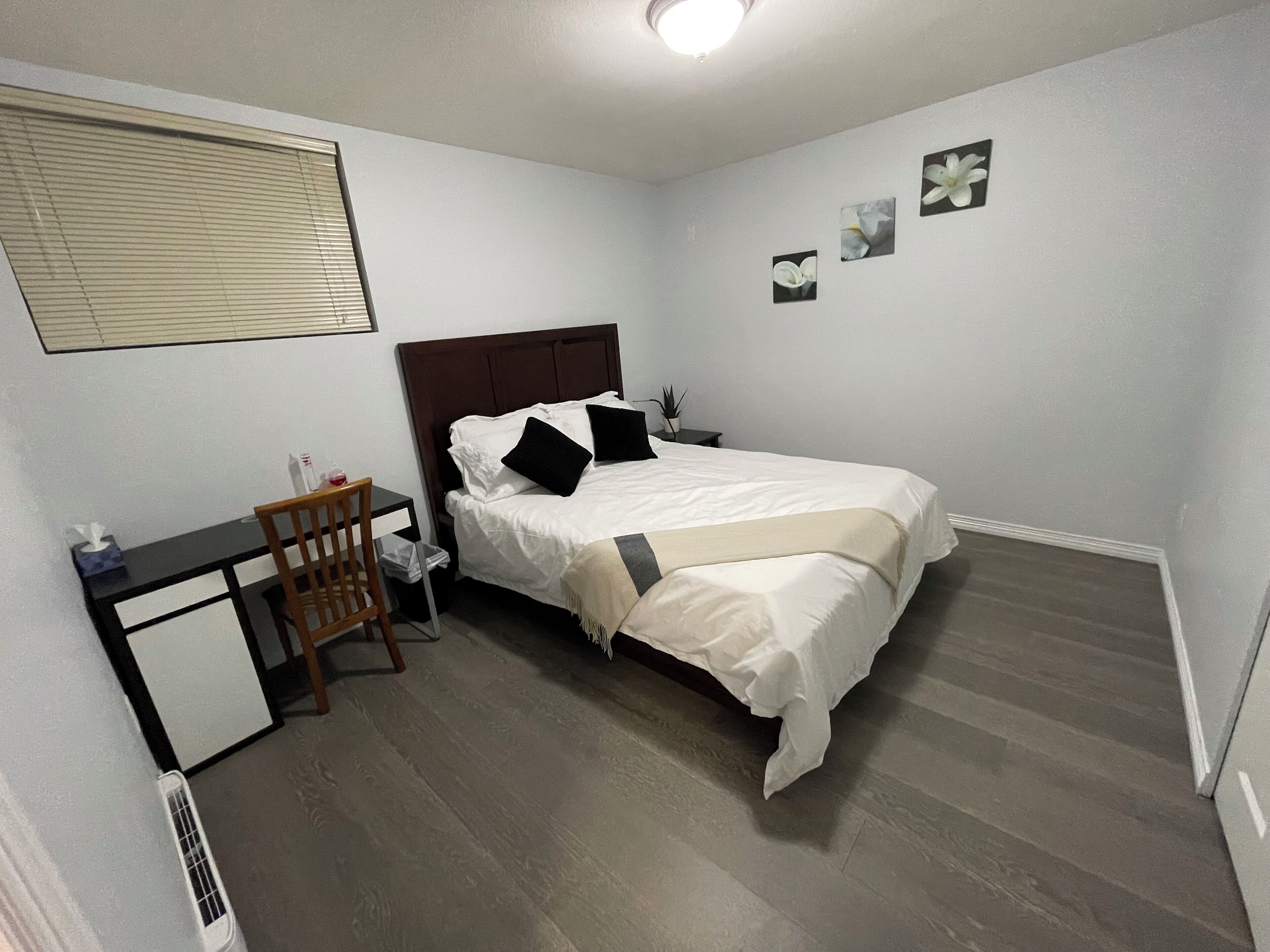 Ein Schlafzimmer mit Bett, Nachttisch, Stuhl und kleinem Schreibtisch mit Pflanze.