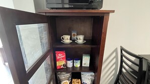 A kitchen area with a microwave on top of a wooden cabinet, shelves with coffee creamer, sugar packets, and a coffee maker. - Spacious Guest Suite in Coquitlam (Coquitlam)