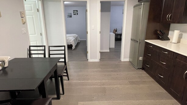 A compact living space with a dining area, kitchenette, and a bedroom visible through an open door. - Spacious Guest Suite in Coquitlam (Coquitlam)