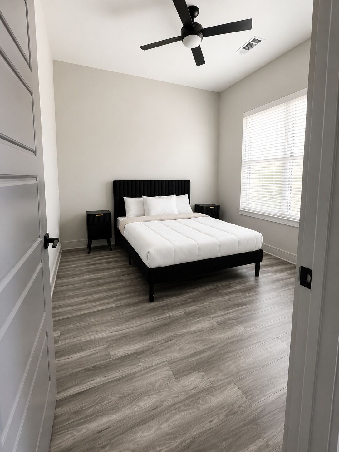 Une chambre à coucher avec un lit, un ventilateur de plafond, une fenêtre avec des stores et une porte.
