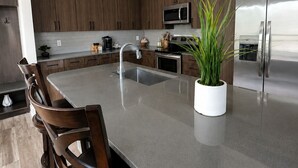 Een moderne keuken met een centraal eiland, donkere houten kastjes, roestvrijstalen apparatuur en hangende lampen.