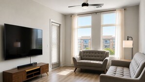 Een moderne woonkamer met een flatscreen televisie, een houten tv-meubel, twee banken en grote ramen met zonwering.