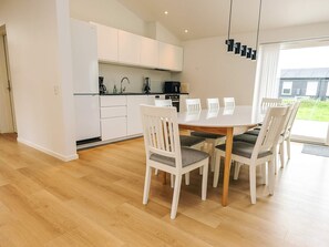 A modern kitchen with white cabinets, a dining table with chairs, and a view of the outside. - 5 Star Holiday Home in Saltum (Saltum)