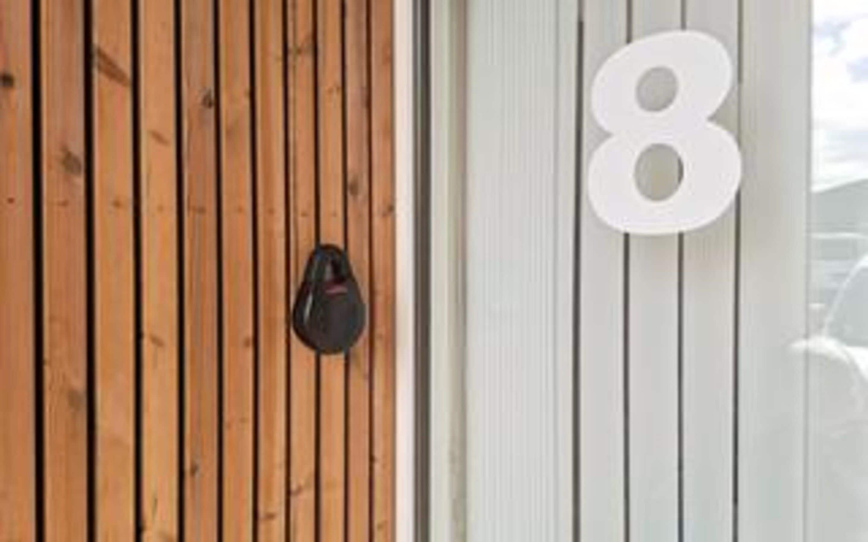 Una puerta de madera con un bolso negro colgado de un gancho, y un letrero blanco con el número 8.