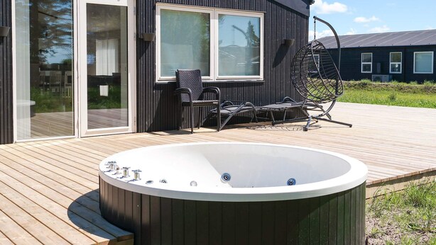 A modern building with a wooden deck, a hot tub, outdoor seating, and large windows. - 5 Star Holiday Home in Saltum (Saltum)