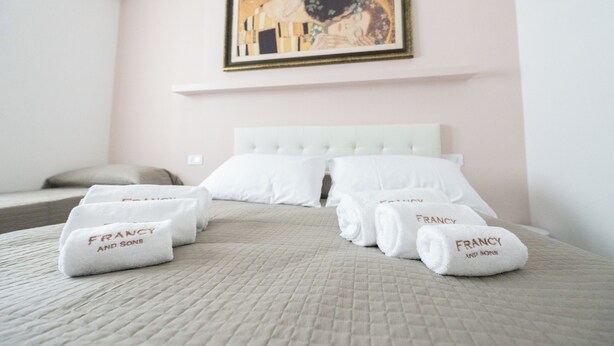 Ett hotellrum med en säng, kuddar och handdukar, alla försedda med logotypen för företaget ”FRANCY AND SONS”.