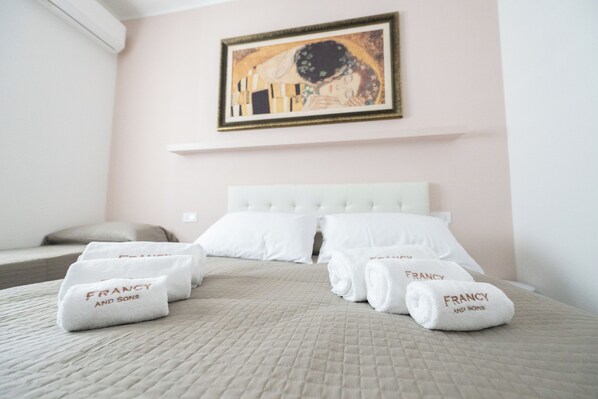 A hotel room with a bed, pillows, and towels with 'FRANCY AND SONS' branding.