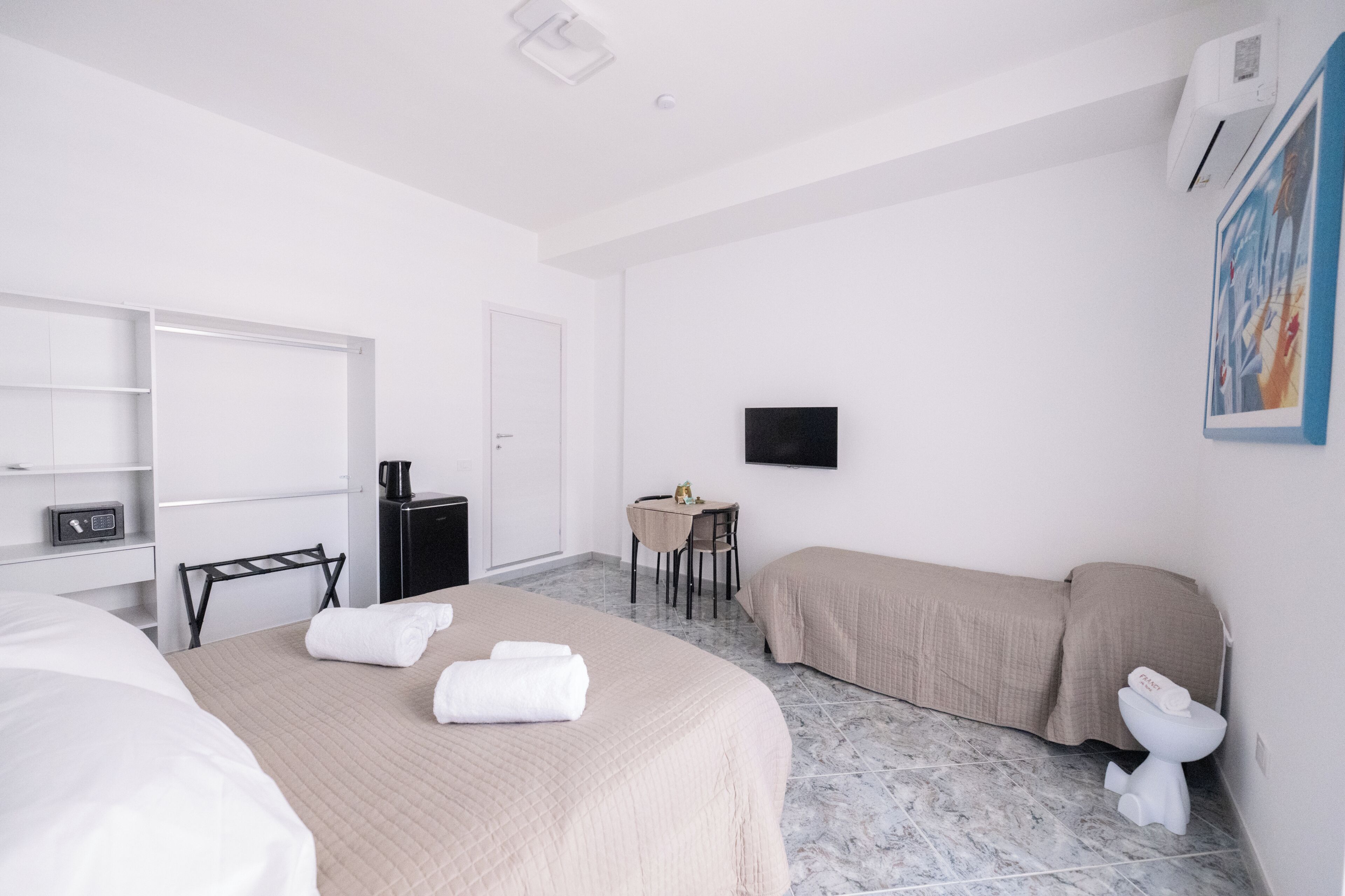 Una camera d'albergo con un letto, una scrivania, una sedia, un divano, una TV, una macchina del caffè e un bagno.