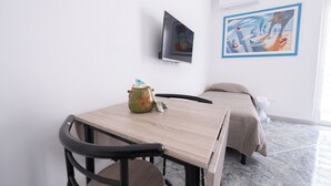 Ett rum med en säng, ett bord, en stol, en tv och en tavla på väggen.