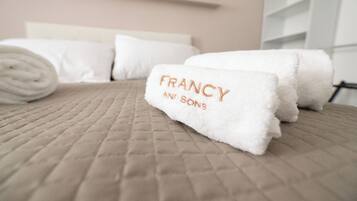 Una cama bien hecha con toallas blancas enrolladas y un texto visible en una de ellas.