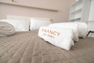 Una cama bien hecha con toallas blancas enrolladas y un texto visible en una de ellas.