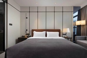 Una habitación de hotel moderna con una cama grande, una mesita de noche, una silla y vistas a la ciudad.