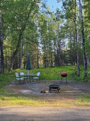 Un camping con mesa y sillas, una parrilla y una tienda de campaña.