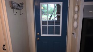 Ein Flur mit einer blauen Tür, einem kleinen Fenster, einem Kleiderständer mit rustikaler Dekoration und einem Kühlschrank.