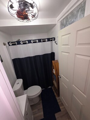 A compact bathroom with a toilet, a shower curtain, and a wooden door. - Whaler's Cove, pleasant 1-bedroom/1 bath apt. in Kenai perfect for your getaway. (Kenai)