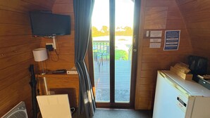 Una habitación con una televisión montada en la pared, un escritorio con una computadora, un refrigerador y una puerta que da a un área exterior con patio.