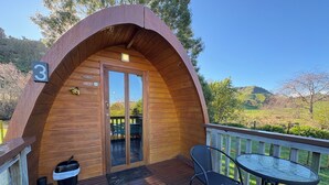 Una cabaña de madera con puerta de vidrio, un letrero con el número 3, una mesa pequeña al aire libre y sillas.