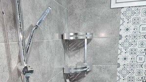 Eine Dusche mit Duschbrause, Wandarmatur und Seifenspender.