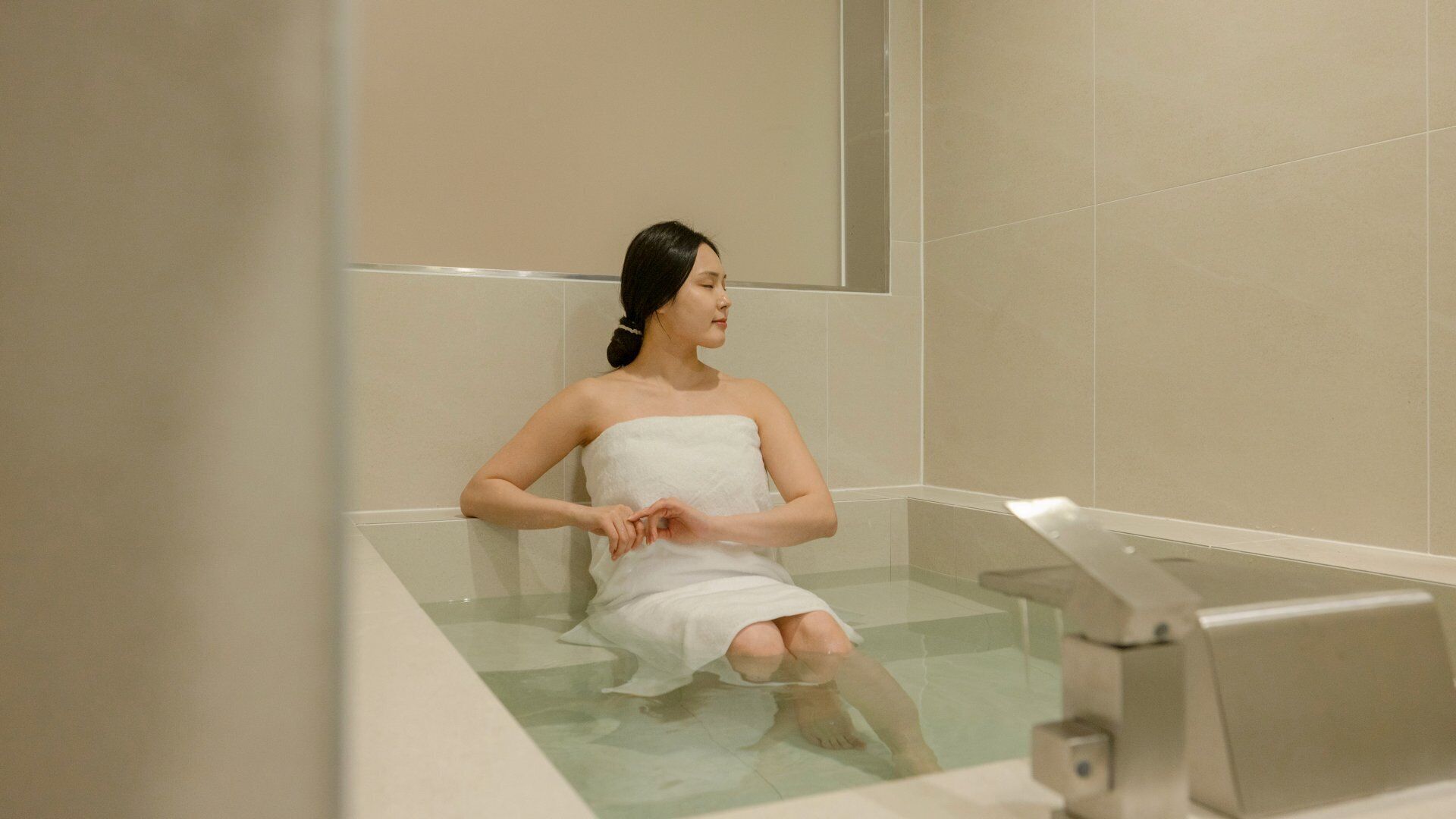 A person sitting in a bathtub with a towel wrapped around their body.